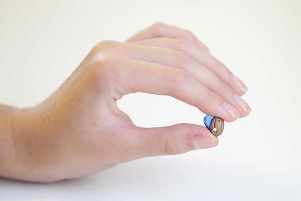 A woman's hand holding a hearing aid that is in for repairs.